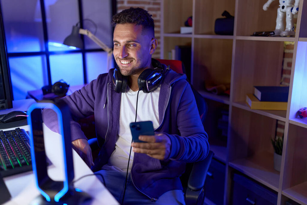 Молодий іспаномовний чоловік стример використовує комп'ютер і смартфон в ігровій кімнаті
 - Фото, зображення