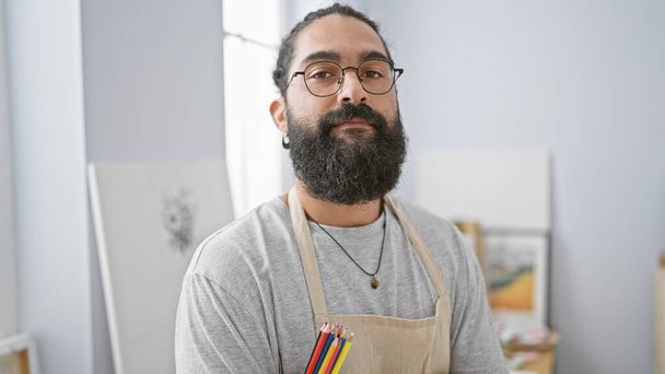 Spaanse man met baard en bril draagt een schort in kunststudio. - Foto, afbeelding