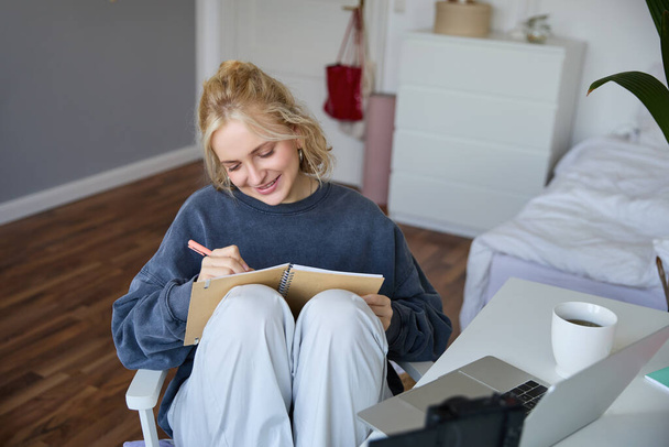Portrait of smiling cute woman, lifestyle blogger, sits in her room with daily journal or planner, records video on digital camera, creates content for social media about daily routine. - Photo, Image