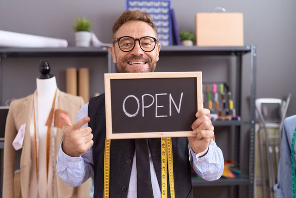 Middle age man with beard dressmaker designer holding open sign smiling happy pointing with hand and finger  - Photo, Image