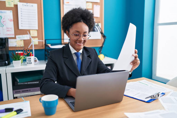 アフリカ系アメリカ人の女性ビジネスワーカーがオフィスでノートパソコン読み取り文書を使う - 写真・画像