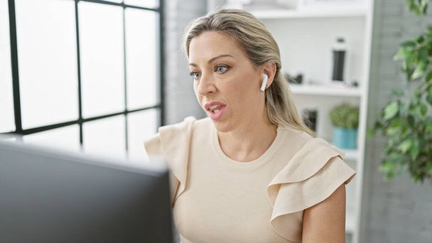 Nuori blondi nainen liiketoiminnan työntekijä, joka käyttää tietokonetta ja kuulokkeita töissä toimistossa - Valokuva, kuva