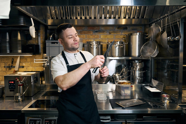 Кавказький чоловічий шеф-кухар точильний ніж з точилкою на кухні в ресторані. Концепція смачного здорового харчування - Фото, зображення