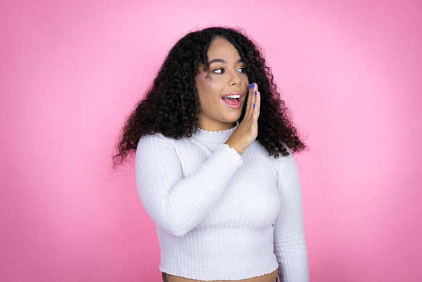 アフリカ系アメリカ人女性は,秘密の噂を口にピンクの背景の手の上にカジュアルなセーターを着て,悪意のある話し合いを囁きます - 写真・画像