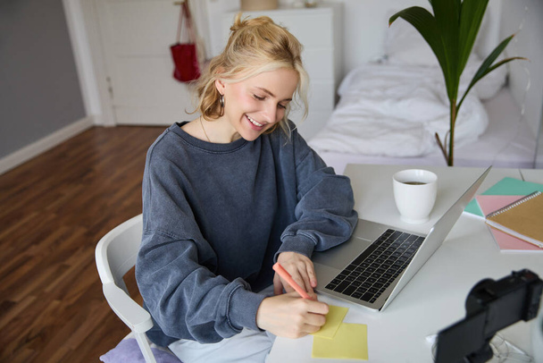 Retrato de una mujer joven aprendiendo a distancia, trabajando desde casa con el ordenador portátil, tomando notas, estudiante estudiando a distancia, haciendo curso en línea. - Foto, imagen