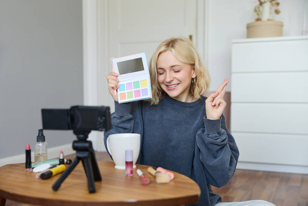 Portret van mooie lifestyle blogger, meisje neemt een video op haar camera voor sociale media, toont palet van oogschaduwen, doet een make-up tutorial voor haar volgelingen, zit in haar kamer. - Foto, afbeelding