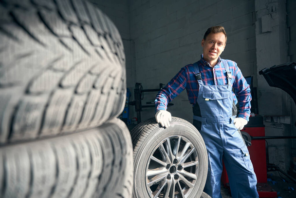 Mechanic in protective uniform and gloves standing near wheel, working and performing repair in tire fitting - Photo, Image