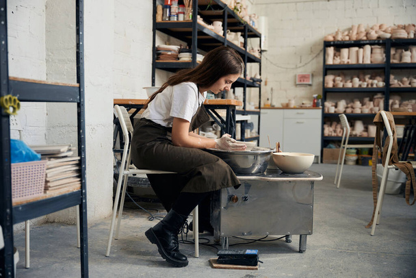 Концентрированная женщина делает горшок с помощью гончарного круга в творческой студии - Фото, изображение