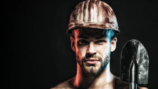 Close-up portret van ernstige professionele bouwer in beschermende helm met spade. Zware industrie en mijnbouw. Mannelijke industriële werknemer of mijnwerker in veiligheid harde hoed met schop. Kopieerruimte voor reclame - Foto, afbeelding