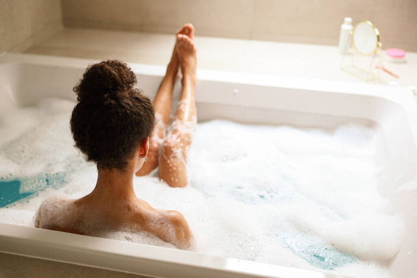 Une femme se baigne tranquillement dans une baignoire en matériau composite, entourée de bulles et d'eau chaude. Elle s'amuse dans la salle de bain - Photo, image