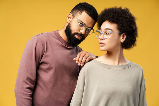 Attractive, fashion African American couple, models wearing stylish eyeglasses posing together isolated on yellow background. Handsome boyfriend and girlfriend together. Concept of vision, health care - Photo, image