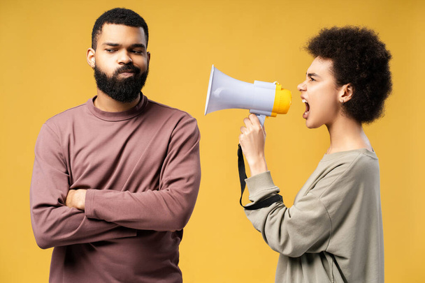 Нещасна пара, афроамериканка, що тримає гучномовця, свариться, кричить, стоячи ізольовано на жовтому тлі. Поняття образливих стосунків - Фото, зображення