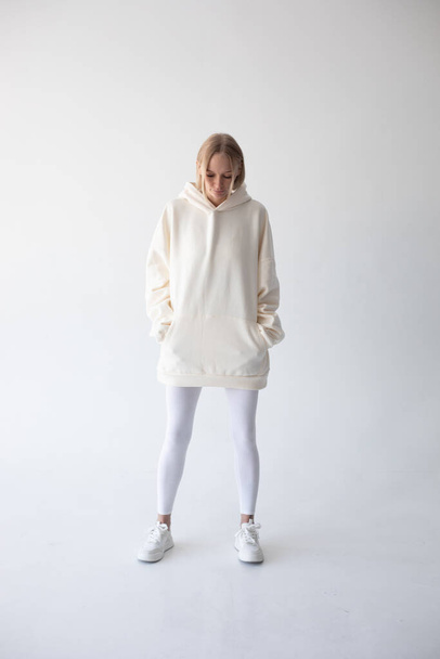 Blonde girl in a white hoodie and tights posing on a white background. High quality photo - Fotó, kép