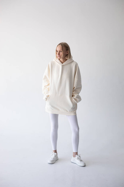 Blonde girl in a white hoodie and tights posing on a white background. High quality photo - 写真・画像