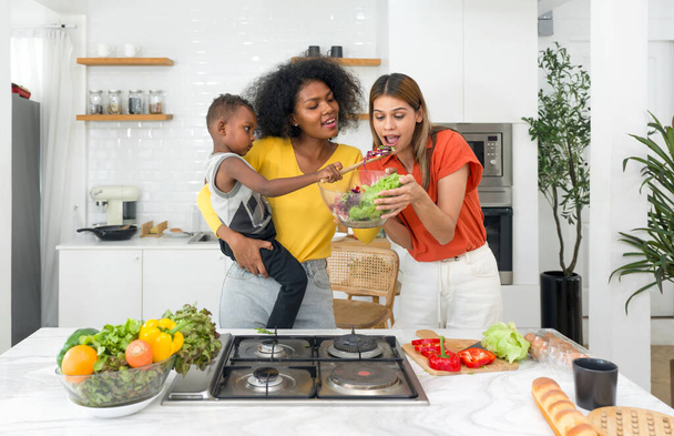 Две женщины и ребенок готовят вместе на хорошо освещенной, домашней кухне, стоя перед современной плитой, олицетворяя единство, любовь и традиции. - Фото, изображение