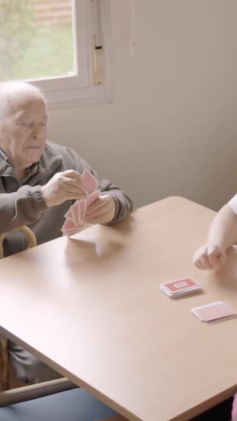 Vídeo en cámara lenta con vista elevada de personas mayores y cuidador jugando a las cartas en un hogar de ancianos - Imágenes, Vídeo