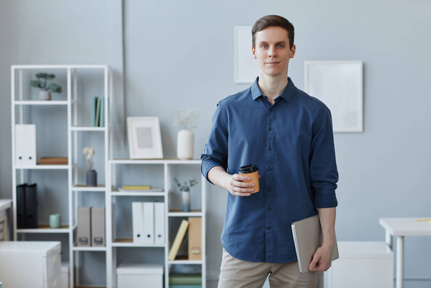 Retrato de cintura hacia arriba del joven empresario exitoso mirando la cámara mientras está parado junto al lugar de trabajo en la oficina, espacio para copiar - Foto, Imagen