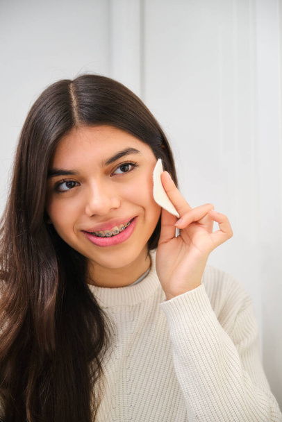 Female Latin teenager with braces using make up cotton pad. - Photo, Image