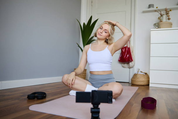 Portrait of young woman personal yoga instructor, recording workout video at home, using digital camera to vlog her exercises, using rubber mat. - Photo, Image