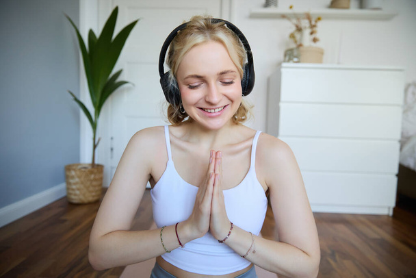 Beeld van jonge vrouw luistert naar yoga podcast voor beginners, houdt hand in hand naambordje, draagt koptelefoon, mediteert. - Foto, afbeelding
