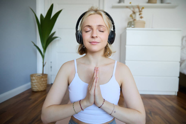 Portret van een vrouw die thuis mediteert, in een koptelefoon zit, naar yoga podcast luistert, handjes in een naambordje houdt. - Foto, afbeelding