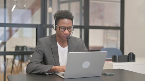 Hombre afroamericano con auriculares mirando a la cámara mientras trabaja en el ordenador portátil - Imágenes, Vídeo