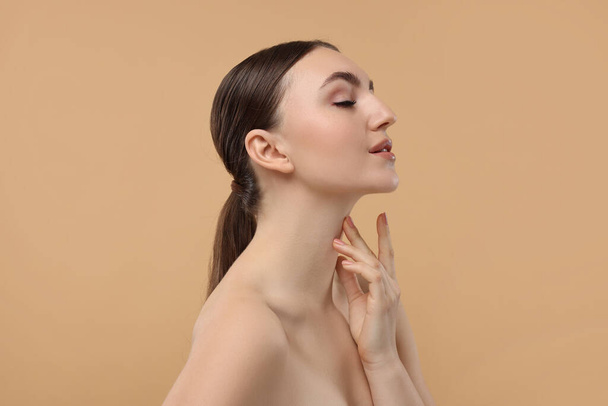 Beautiful woman touching her neck on beige background - Фото, изображение