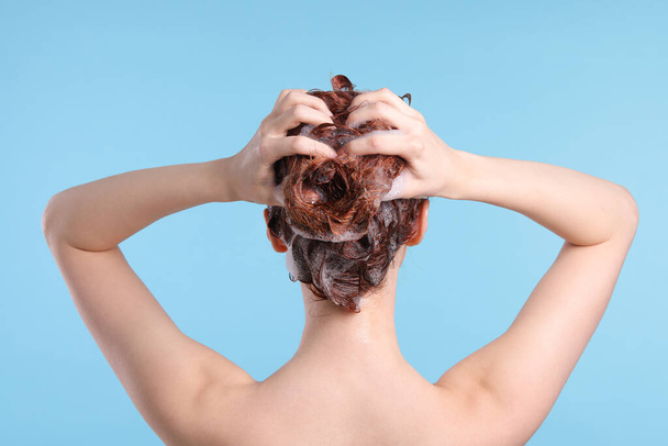 Young woman washing her hair with shampoo on light blue background, back view - Foto, Bild