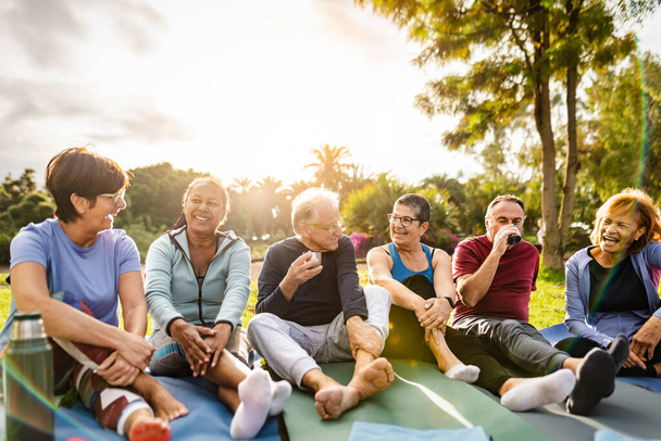 Happy multiracial senior friends drinking a tea after workout activities in a park - Photo, Image