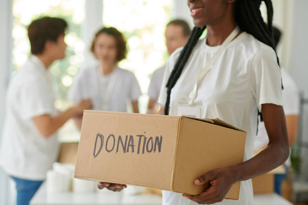Mosolygó fekete fiatal nő gazdaság doboz adományozott élelmiszer vagy ruhák - Fotó, kép