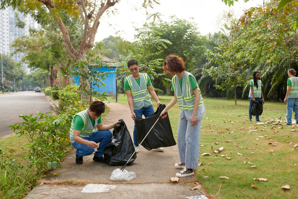 Group of students in vests cleaning local park from garbage - Fotó, kép