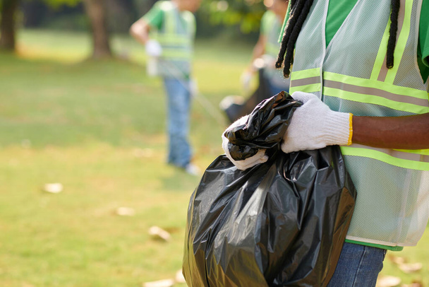Cropped image of eco-volunteer holding black bag with garbage she collected in park - Photo, image