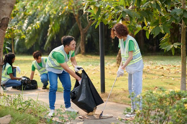 Young people volunteering in park, collecting garbage and fallen leaves - Foto, afbeelding