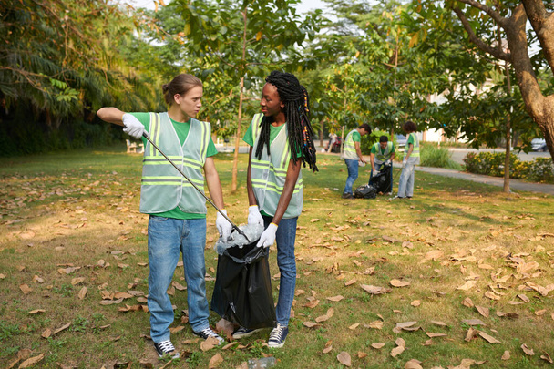 Diverse young couple volunteering in park, collecting garbage in bags - Fotoğraf, Görsel