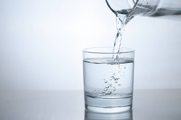 Woda oczyszczona wylewa się z szklanej dzbanek do szklanki. - Zdjęcie, obraz