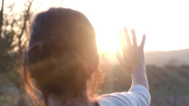 Kobieta trzymająca dłoń przy świecącym słońcu w niewyraźnym krajobrazie rolniczym - Materiał filmowy, wideo