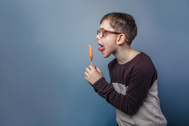 Europese uitziende jongen van tien jaar in glazen likken een lolly - Foto, afbeelding