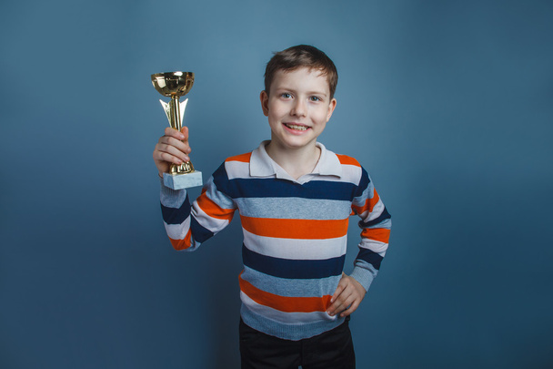 European-looking boy of ten years holding a cup award on a gray - Photo, Image