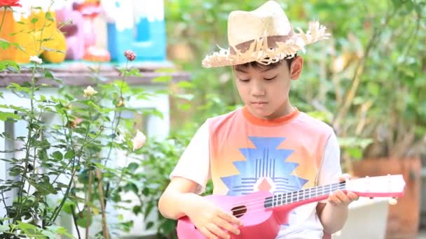 Asijské dítě sedí na mini židli a hraní na kytaru - Záběry, video