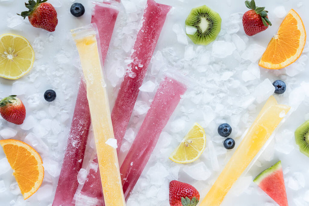 Acima vista de frutas caseiras congelados com gelo e pedaços de frutas espalhados ao redor.  - Foto, Imagem