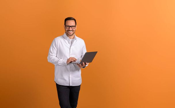 Portrait of confident businessman doing online research over wireless computer on orange background - Photo, Image
