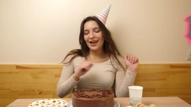 Una chica se sienta frente a una mesa con un pastel festivo, en el que se pega una vela en forma de número 18. El concepto de una celebración de cumpleaños. - Imágenes, Vídeo