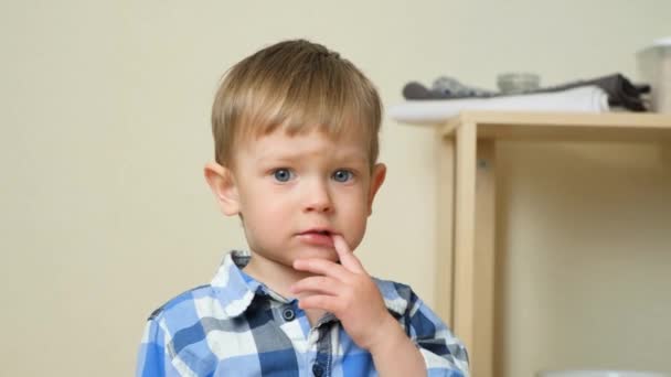 2歳のかわいい男の子が口に指を持ち,カメラを見ている - 映像、動画