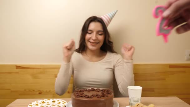A girl sits in front of a table with a festive cake, into which a candle in the form of the number 22 is stuck. The concept of a birthday celebration. - Footage, Video