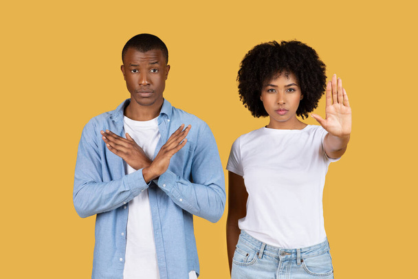 Sérieux homme et femme afro-américain millénaire faisant des gestes d'arrêt avec leurs mains, montrant un refus ou fixant des limites, debout fermement sur un fond jaune - Photo, image