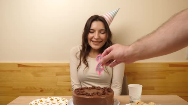 Una chica se sienta frente a una mesa con un pastel festivo, en el que se pega una vela en forma de número 28. El concepto de una celebración de cumpleaños. - Metraje, vídeo