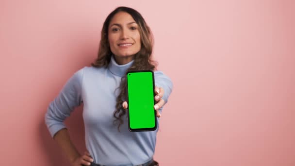 笑顔の女性が保有するモバイルのクロマスクリーンに焦点を当てたピンクの背景のビデオ - 映像、動画