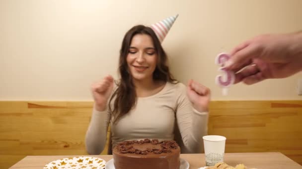 Una chica se sienta frente a una mesa con un pastel festivo, en el que se pega una vela en forma de número 30. El concepto de una celebración de cumpleaños. - Metraje, vídeo