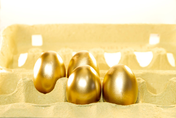 Kartonnen dienblad met gouden eieren, dicht. Verpakking van decoratieve gekleurde eieren voor Pasen. Stijging van de eierprijzen. Voorbereiding van de vakantie - Foto, afbeelding