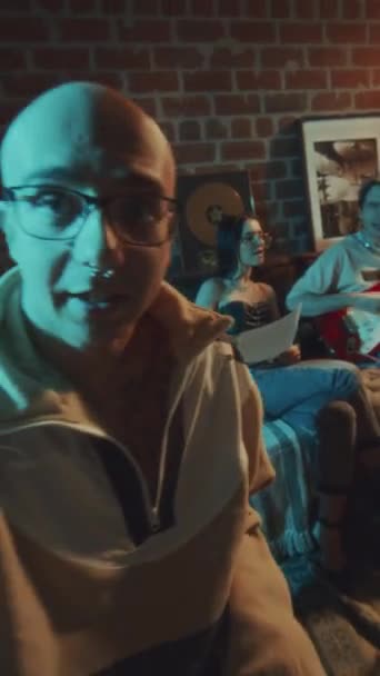 POV UGC séquence verticale de mâle chauve blogueur dans des lunettes enregistrement de ses amis chantant chanson à la guitare en studio rétro et il parle à la caméra dans la soirée - Séquence, vidéo